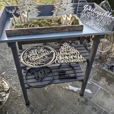 Holztisch mit dekorativen Holzfiguren, Weihnachtsbaum und Schild mit der Aufschrift „Adventsdeko“.