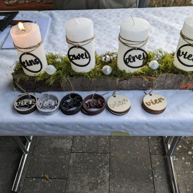 Vier dekorierte Kerzen auf einem Tisch, darunter gravierte Holzuntersetzer.